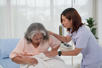 Asian nurse helping a senior Asian female patient with stomach ache on a bed in hospital