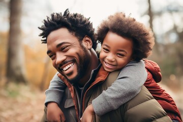 African American father playing and hugging his son in the park. - obrazy, fototapety, plakaty