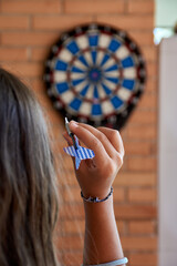 girl with long hair seen from behind while throwing darts at a target