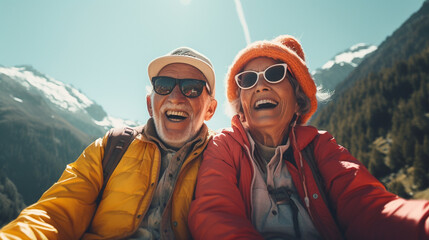 Happy elderly couple laughing on a snowy mountain on a sunny day. They wear warm hats and sunglasses for their excursion, enjoying their retirement and free time