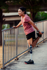 Athlete with prosthetic leg doing warm up exercise on park. Woman wearing prosthetic equipment for...