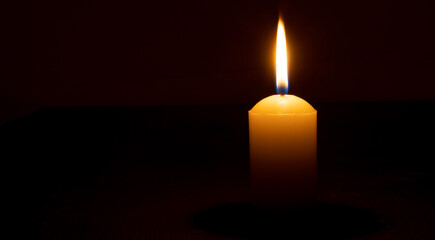 Single burning candle flame or light glowing on a big yellow candle on black or dark background on...