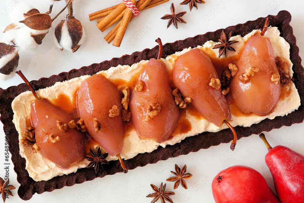 Poster Spice poached pear tart with caramel on a chocolate and cream base. Top view table scene over a white marble background.
