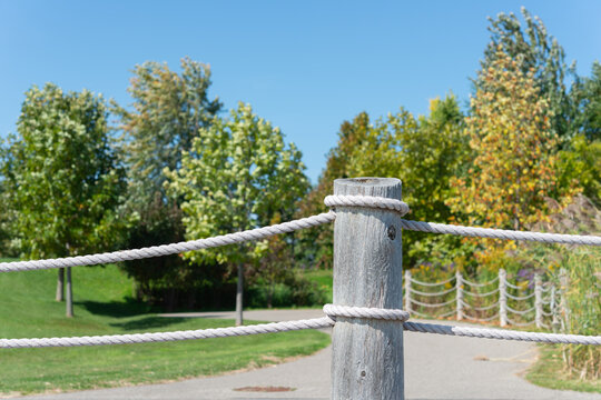 close-up of a nautical themed rope fence with post and trees in the park by the lake
