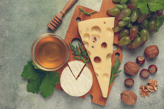 cheese with big holes, emmental, maasdam, brie cheese, on a cutting board, with grapes and honey, nuts, appetizer to wine, top view,
