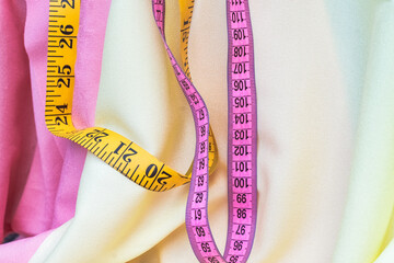 two yellow and pink measuring tapes on soft yellow and pink textile. Weaving concept