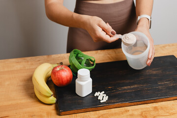 Athletic woman in sportswear with measuring spoon in her hand puts portion of whey protein powder...