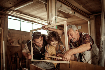 Obraz na płótnie Canvas Multigenerational family of male carpenters teaching their youngest one the ways in a carpentry shop
