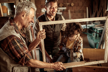 Multigenerational family of male carpenters teaching their youngest one the ways in a carpentry shop