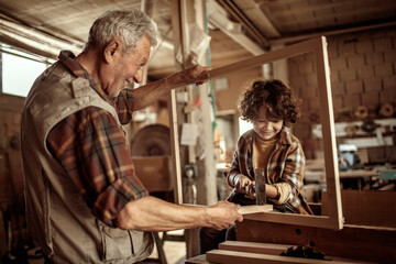 Senior male carpenter teaching his grandson how to use a hammer in a carpentry shop