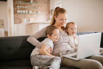 Young mother using the laptop with her children on the couch at home