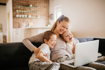 Young mother using the laptop with her children on the couch at home