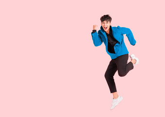 Fototapeta na wymiar Portrait of happy handsome Asian man in a blue jacket excited and celebrating by jumping up in the air with winner gesture isolated on pink background.