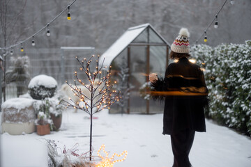 Woman in sleepwear and hat goes out on her snowy backyard in the morning during winter holidays