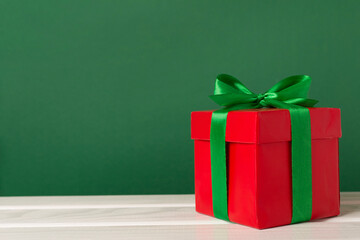 Red gift box with green ribbon and bow on table