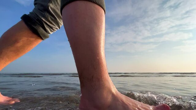 Man walking barefoot on sandy beach at sunset