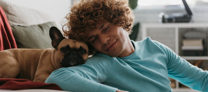 Cute Little Dog Leaning Head On Shoulder Of Young Handsome Man While Both Napping At Home Together