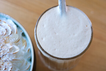 Frappe with sugar syrup coffee with milk delicious drink high foam stir with a straw in a restaurant Glass of a iced coffee with cream milk. Cold brew coffee drink with ice. Early morning sun light. 