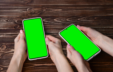 Two female hands holding a cell phone with a green screen