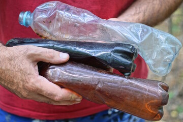 a man in red clothes removes garbage on the street and holds three old dirty plastic bottles in his hands
