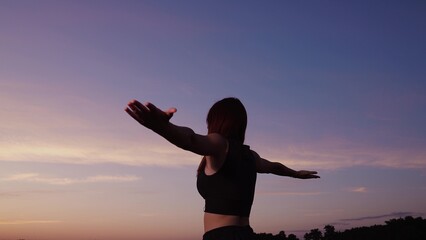 Fototapeta na wymiar Happy woman with spread hands meditates outdoors under colorful sunset sky