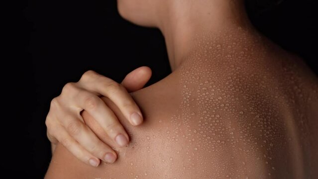 Closeup studio shot of young woman body part, touching her smooth skin with water drops on the shoulder after showering.