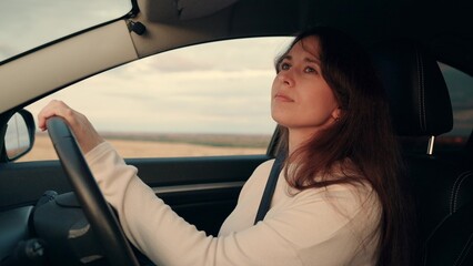 Cheerful young woman drives modern car along rural road at sunset light