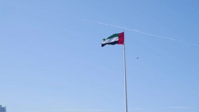 The UAE or United Arab Emirates flag flutters in the wind on a flagpole against a blue sky. UAE National Day.
