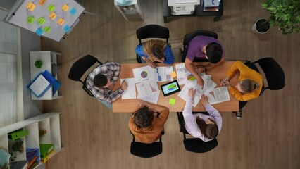 Top view of office boardroom, young male and female workers. Startup company brainstorming discussing ideas, sitting around the desk.