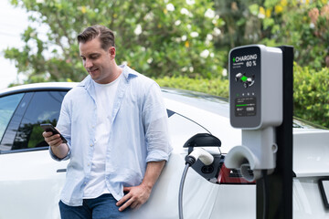 Modern eco-friendly man recharging electric vehicle from EV charging station, using Innovative EV...