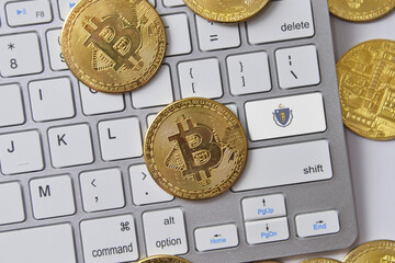 flag of massachusetts state on the keyboard with bitcoin coins on a grey background.