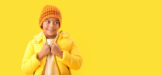 Cute African-American boy in warm winter clothes on yellow background with space for text
