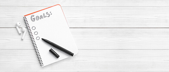 Notebook with empty to do list, marker and earphones on white wooden background with space for text. New year goals