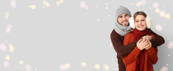 Happy young couple in winter clothes on light background with space for text