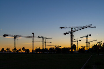 Silueta de conjunto de torres de grúas al atardecer en un terreno donde se están realizando obras...