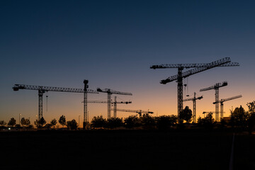 Silueta de conjunto de torres de grúas al atardecer en un terreno donde se están realizando obras...
