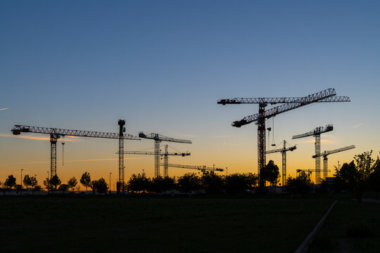 Silueta de conjunto de torres de gr&uacute;as al atardecer en un terreno donde se est&aacute;n realizando obras de construcci&oacute;n de edificios residenciales.