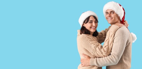 Happy young couple in Santa hats and warm sweaters on light blue background with space for text