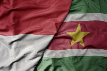 big waving realistic national colorful flag of indonesia and national flag of suriname .