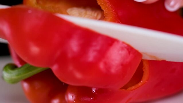 Professional cook in gloves cuts ripe red bell pepper with water drops on brown wooden board in restaurant extreme closeup. High quality 4k footage