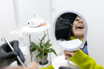 Reflection in mirror of mouth of young woman being examined by dentist