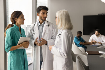 Diverse group of practitioners in white uniform coats discussing medical profession, doctor...