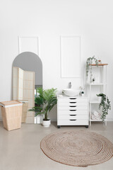 Interior of bathroom with chest of drawers, shelving unit, mirror and laundry basket