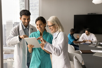 Positive healthcare workers in white uniform coats using digital tablet for effective cooperation, teamwork, discussing patient case, medical conference, medical online application for job