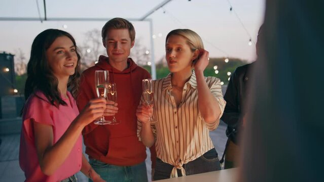 Diverse youngsters toasting drinks in sunset bar terrace. Friends celebrating