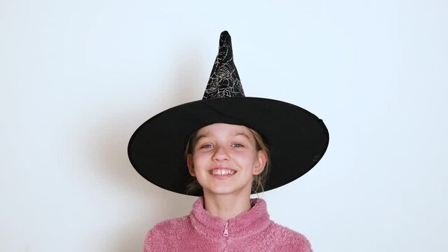 A teen blond girl in black witch hat is actively telling something and looking at the camera. The girl sings or recites a poem. Video portrait. 4k resolution video