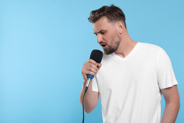 Naklejka premium Handsome man with microphone singing on light blue background. Space for text