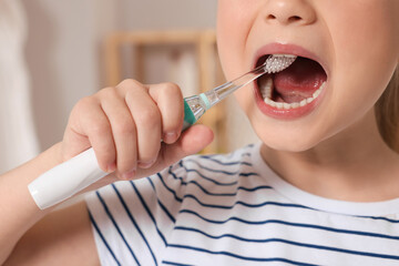 Little girl brushing her teeth with electric toothbrush indoors, closeup