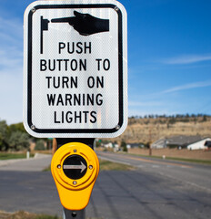 A white sign informing pedestrians to push a button to activate warning lights so they can safely cross the street. 