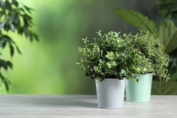 Different artificial potted herbs on white wooden table outdoors, space for text